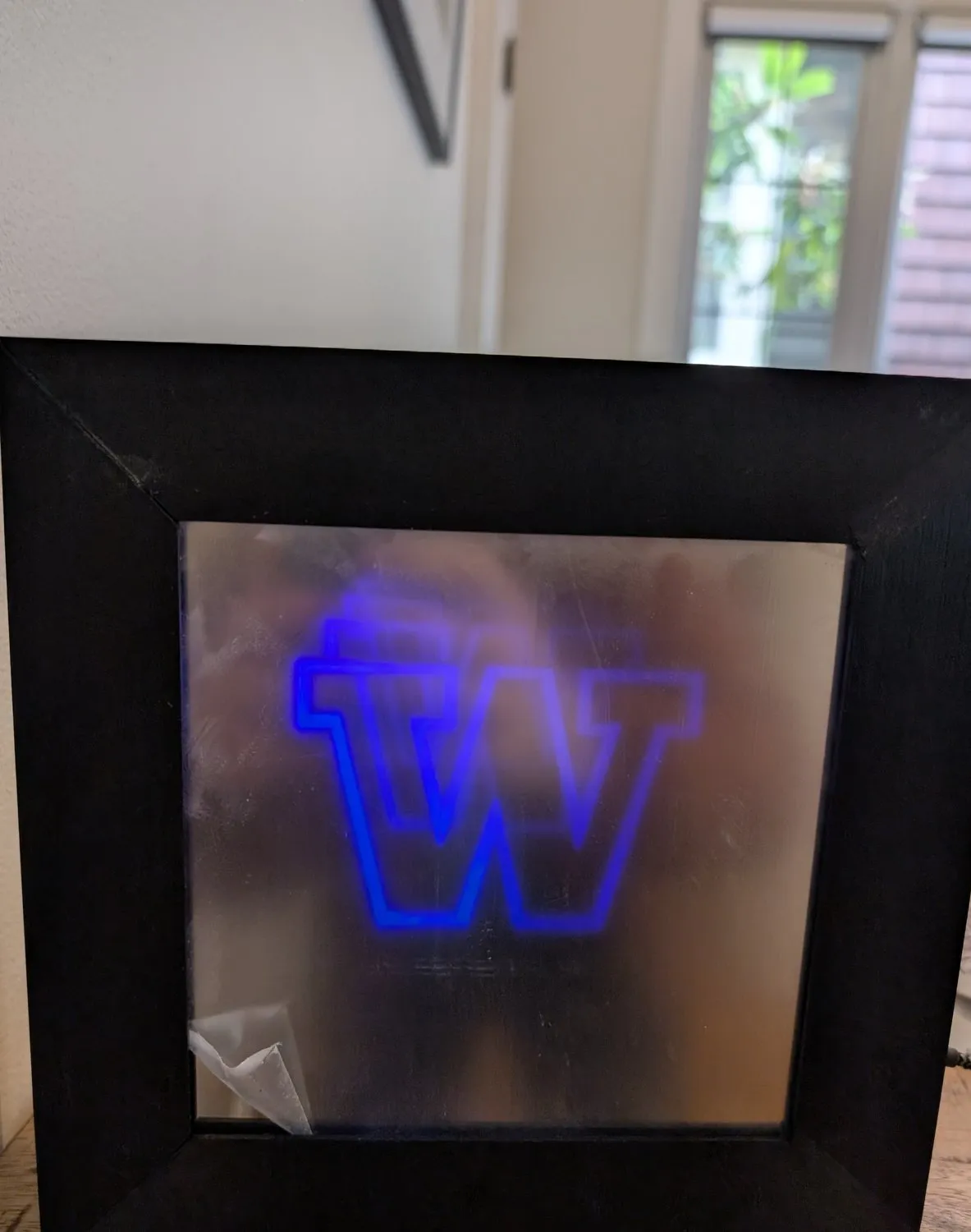The six-inch mirror in a black frame on a table, its custom W glowing violet and receding into an apparent tunnel of light