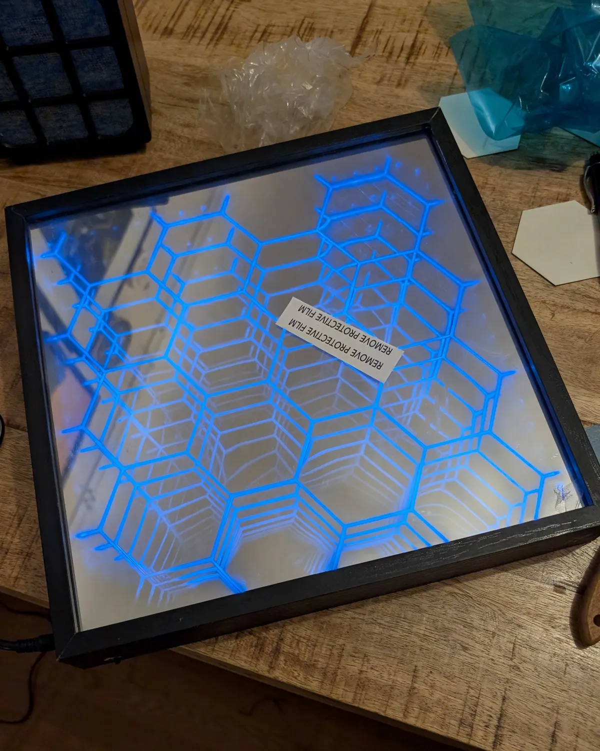 The lit 3D-printed hexagonal structure assembled inside the shadow box on the workbench