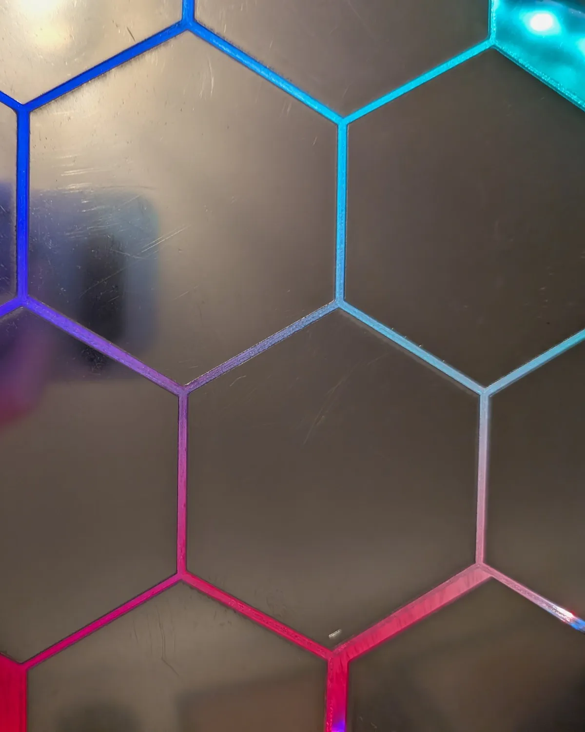 Macro of the lit hexagonal surface, individual cells glowing cyan, blue, and magenta