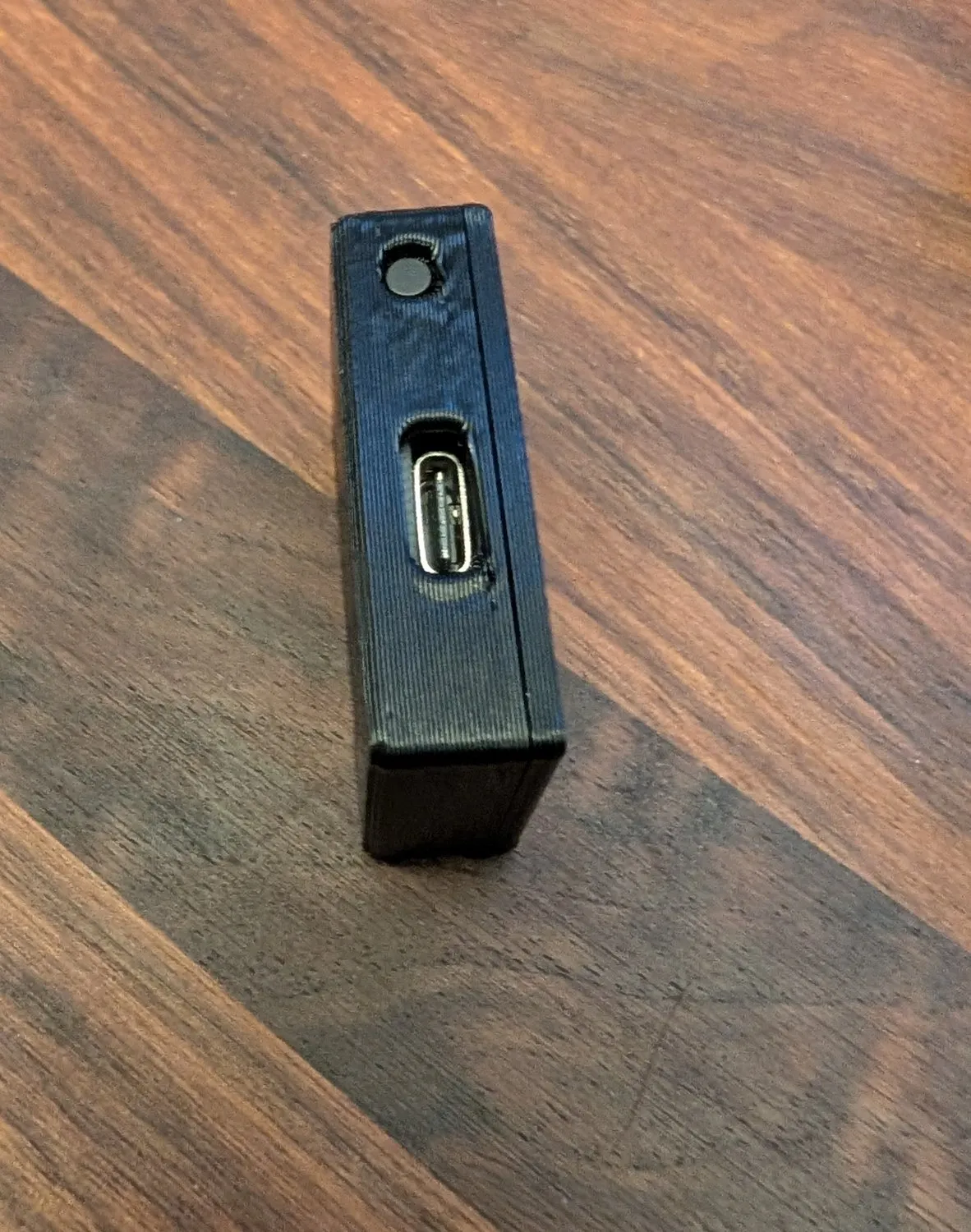 The small black 3D-printed controller enclosure on a desk, showing its USB-C port and a single button