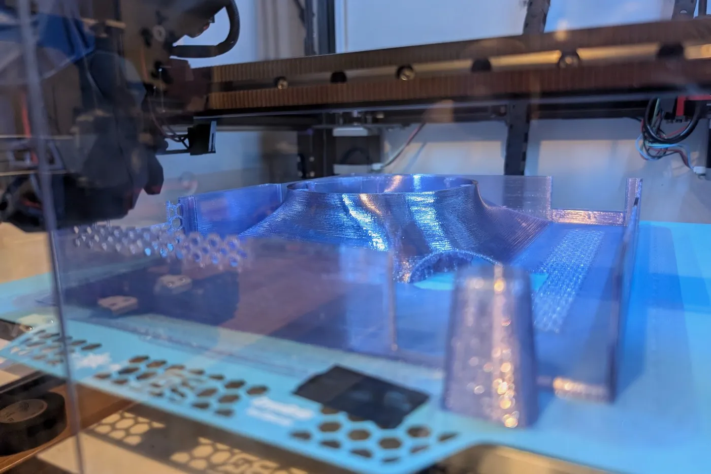 A case panel printing on the 3D printer bed under blue light