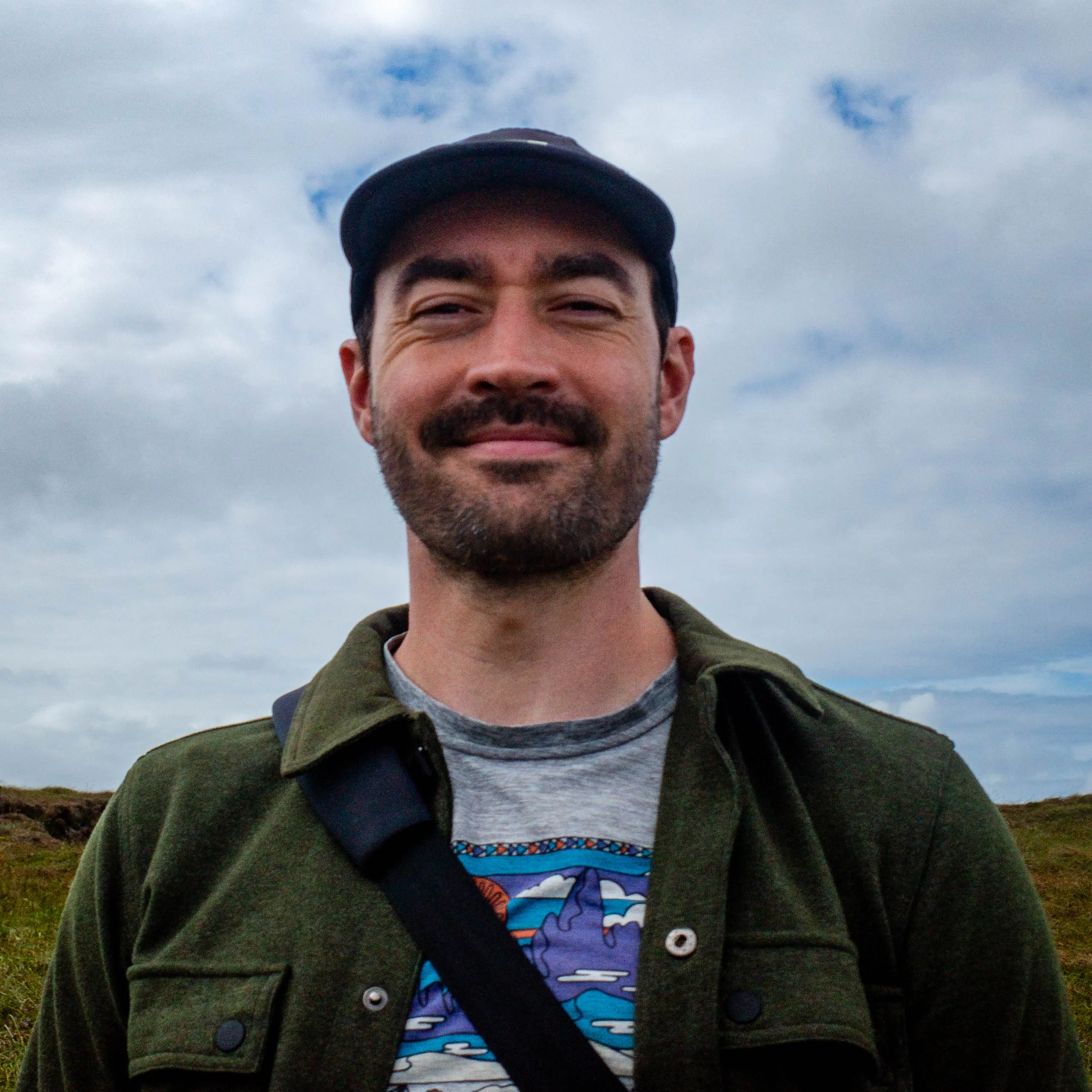 Bill White, smiling outdoors in a cap with an overcast sky behind him